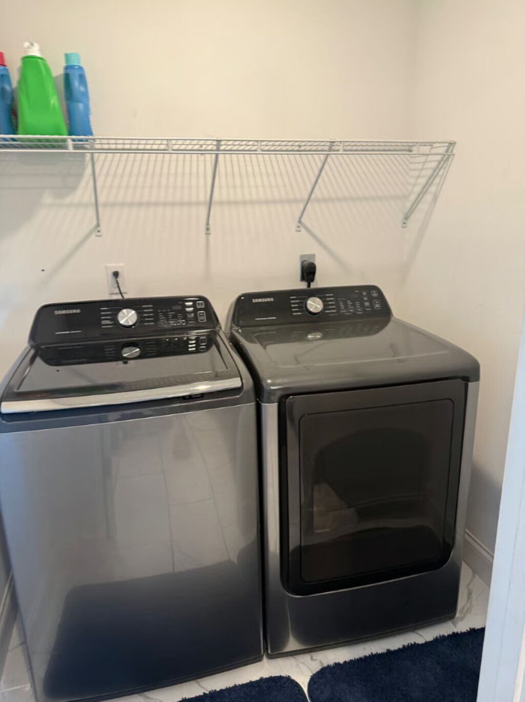 A laundry area with two front-loading washing machines and a metal shelf above them.