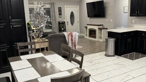 A spacious living room with a fireplace, a dining area with a table and chairs, and a kitchen with dark cabinets and a flat-screen TV. - The Gilliam House (london)