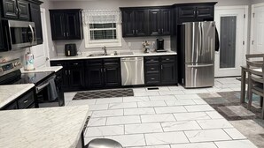 A modern kitchen with dark cabinetry, stainless steel appliances, and a tiled floor. - The Gilliam House (london)