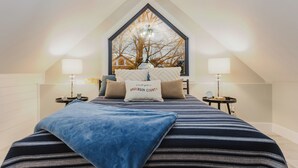 A bedroom with a large window, a bed with striped bedding, two bedside tables with lamps, and a pillow with "Anderson County" text.