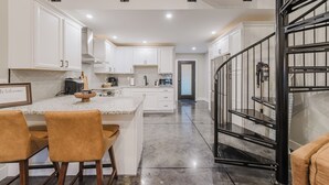 A modern kitchen with white cabinetry, a central island with bar stools, and a staircase with a metal railing.