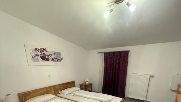 A bedroom with two single beds, a ceiling fan, a radiator, a window with a curtain, and a framed picture on the wall. - Attika Hotel (Halstenbek)