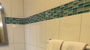 A bathroom with a white sink, two bottles of hand soap, a glass shower enclosure, a white towel rack, and a white radiator. - Attika Hotel (Halstenbek)