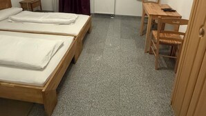 A small, clean room with two wooden beds, a wooden table, a chair, a radiator, and a ceiling fan. - Attika Hotel (Halstenbek)