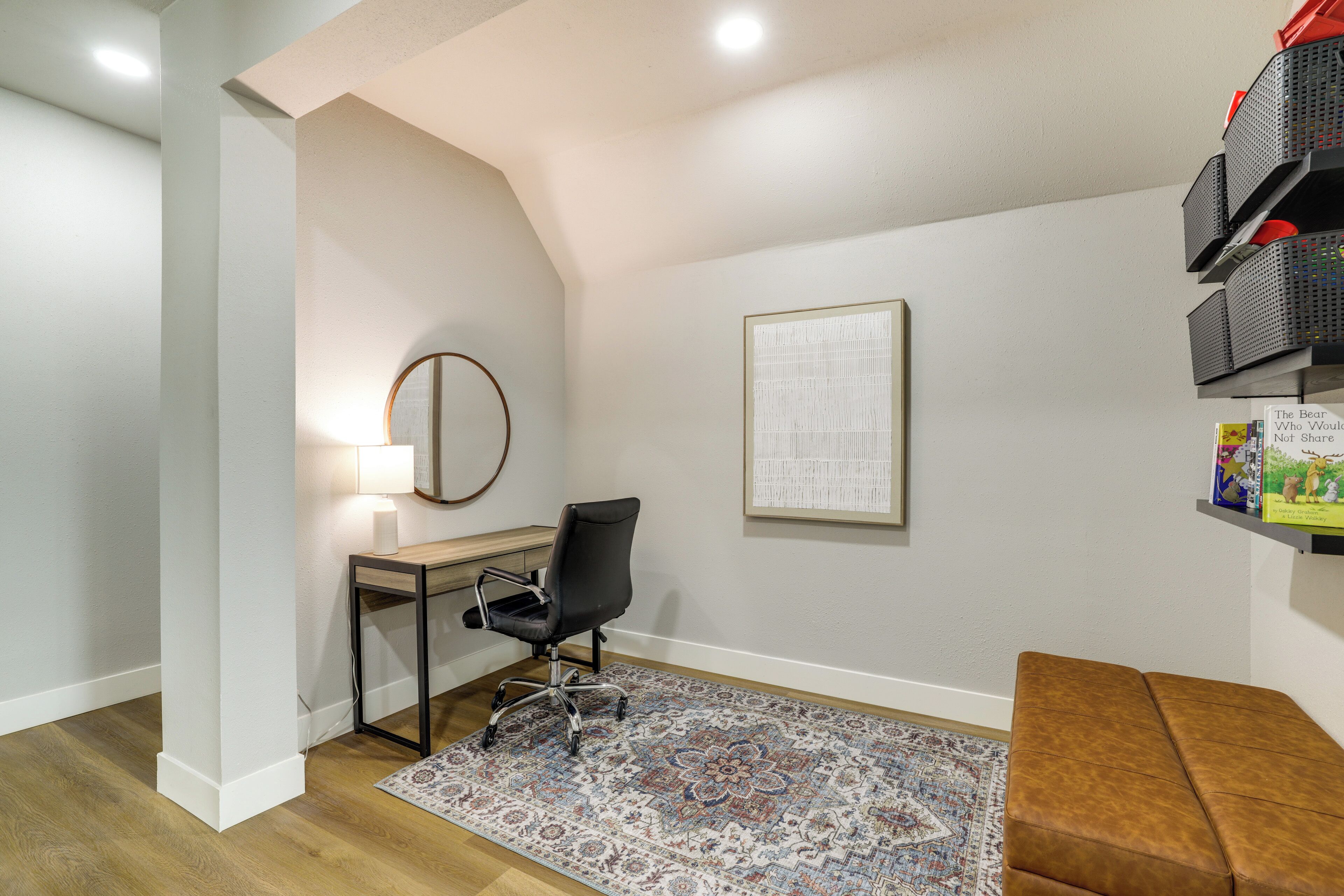 A room with a desk, chair, rug, and a brown bench.