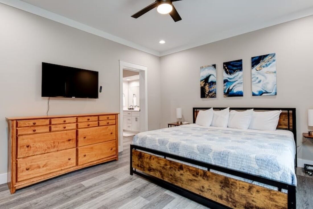 Une chambre à coucher comprenant un lit, une commode en bois, un téléviseur et des œuvres d’art abstraites accrochées au mur.