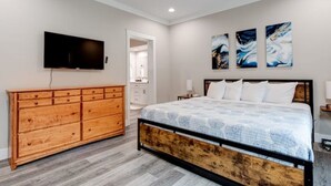 A bedroom with a bed, a wooden dresser, a television, and abstract wall art.