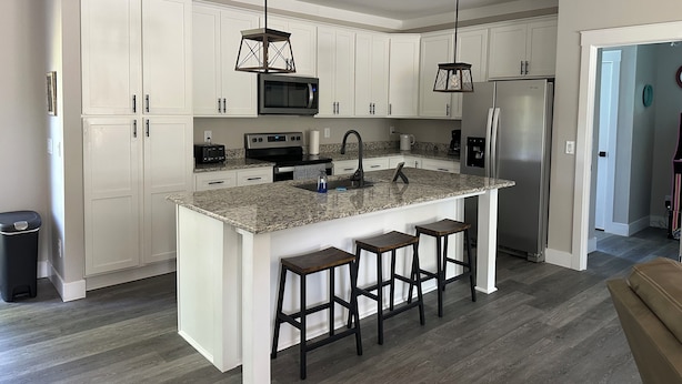 A modern kitchen with white cabinets, granite countertops, stainless steel appliances, and a central island with bar stools.