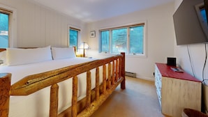 Een slaapkamer met een houten bedframe, een nachtkastje met een lamp, en een televisie op een dressoir.