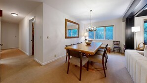 Een eetkamer met een houten tafel, stoelen, een kroonluchter, een grote spiegel en een raam met uitzicht op bomen.