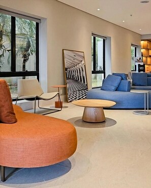 A modern living room with a round wooden coffee table, a blue sofa with cushions, and a large abstract painting on the wall. - Luxury suite 5 minutes from Congonhas Airport, queen-size bed + single bed (São Paulo)