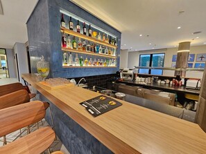 A bar area with a wooden counter, bar stools, a variety of liquor bottles, a coffee machine, and a view of the outdoors through the window. - Luxury suite 5 minutes from Congonhas Airport, queen-size bed + single bed (São Paulo)