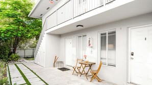 Un edificio bianco con un balcone, un piccolo patio con tavolo e sedie, e un tappetino d'ingresso con la scritta 'hello'.