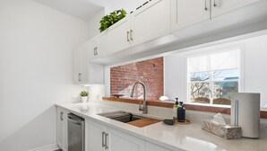 Eine moderne Küche mit weißen Schränken, einer Ziegelrückwand, einer Edelstahl-Spüle und einem Fenster mit Ausblick.
