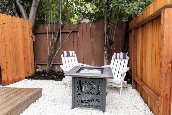 A patio with two Adirondack chairs, a square table, and a wooden deck.