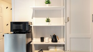 Een compacte leefruimte met een kitchenette, inclusief een koelkast, magnetron en koffiezetapparaat op een plank.