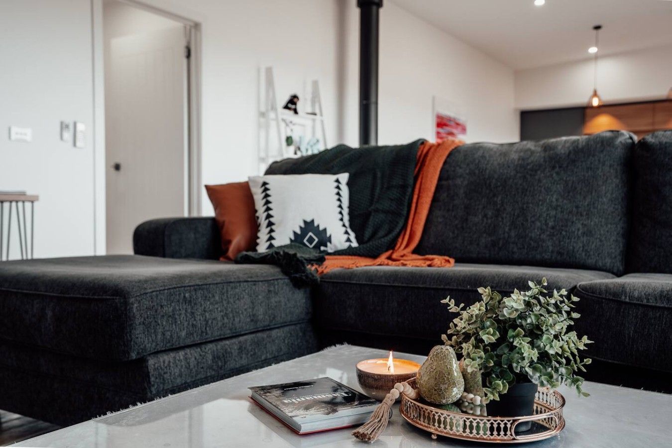Een moderne woonkamer met een donkergrijze bank, een klein tafeltje met een boek, een kaars en een decoratieve plant.