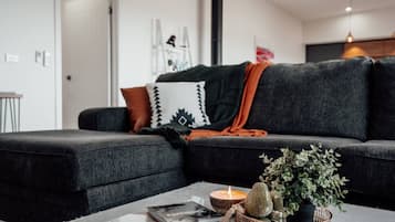 Een moderne woonkamer met een donkergrijze bank, een klein tafeltje met een boek, een kaars en een decoratieve plant.