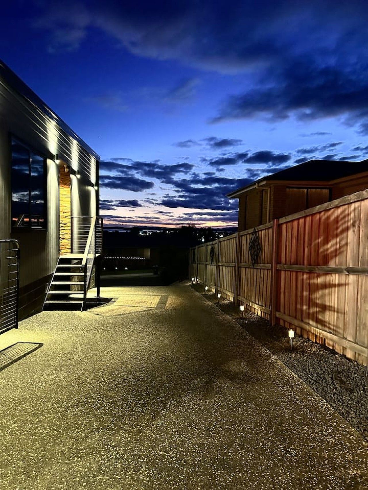 A gravel driveway leading to a building with a staircase and a wooden fence.