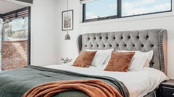 Een slaapkamer met een gestoffeerd hoofdeinde, een groot raam en uitzicht op het omliggende landschap.