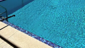 Ein klares, blaues Schwimmbecken mit Liegestühlen und Palmen.