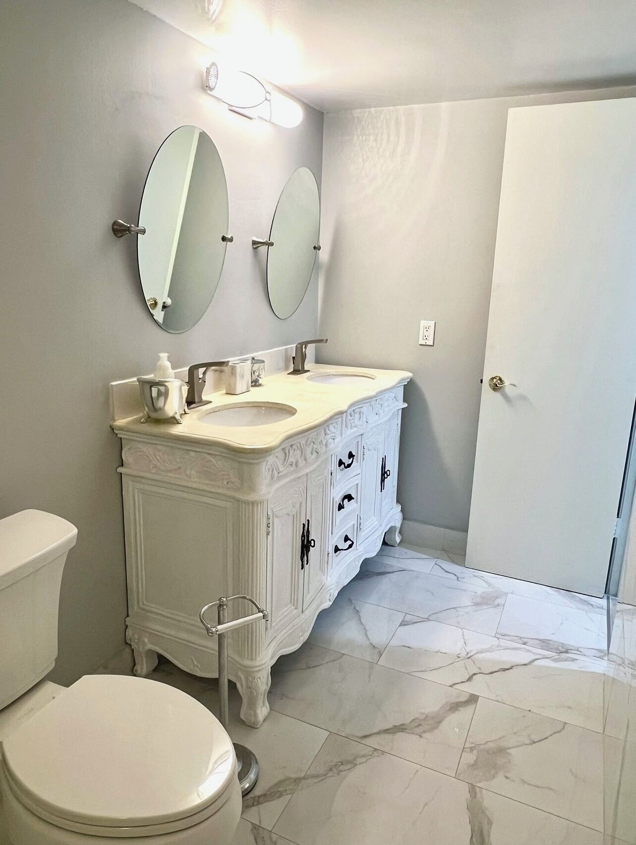 A bathroom with a white vanity, two mirrors, a toilet, and a door.