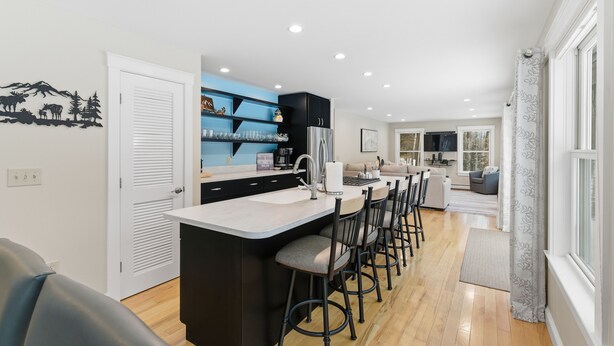 A modern kitchen with a central island, bar stools, and a dining area with a sofa and chairs. - Enjoy private and pristine access to the Pemigewasset River from THE RIVER VIEW… (Campton)