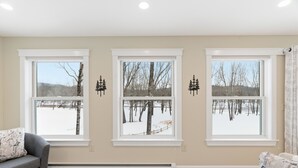 A room with three large windows, a gray sofa, and a patterned rug. - Enjoy private and pristine access to the Pemigewasset River from THE RIVER VIEW… (Campton)