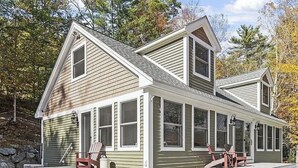 A two-story house with a covered porch, steps leading to the entrance, and two Adirondack chairs on the porch. - Enjoy private and pristine access to the Pemigewasset River from THE RIVER VIEW… (Campton)