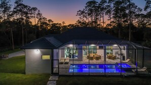 A modern house with a glass-enclosed pool area, outdoor seating, and a well-maintained lawn. - The Naples Luxe Retreat . Game Room • Heated Pool (Naples)