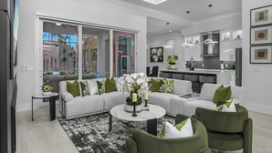 A modern living room with a sectional sofa, green armchairs, a coffee table, and a view of the city through large windows. - The Naples Luxe Retreat . Game Room • Heated Pool (Naples)