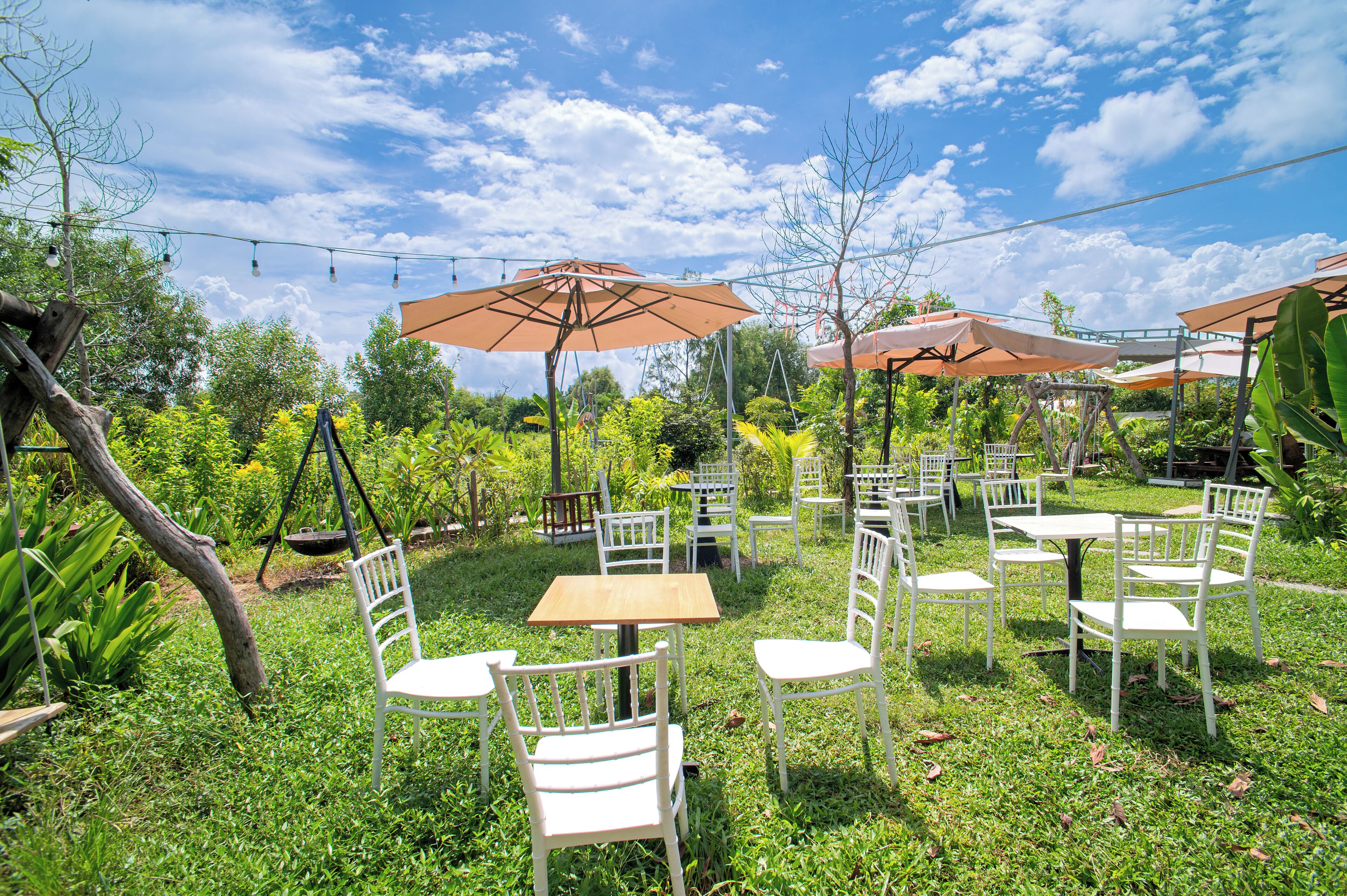 An outdoor seating area with tables and chairs, surrounded by greenery and under umbrellas.