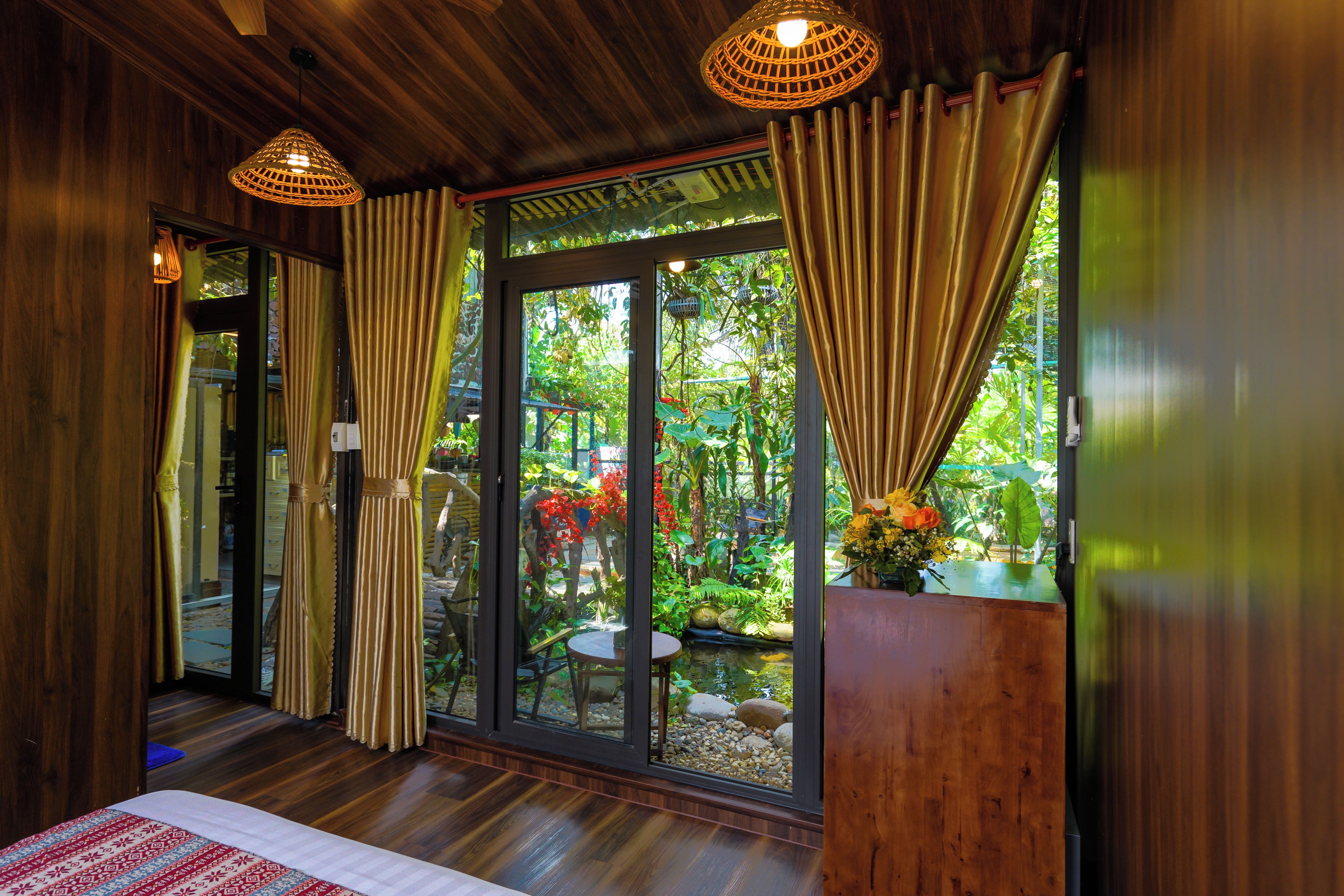 A room with wooden walls, a bed, a window with curtains, and a view of a garden.