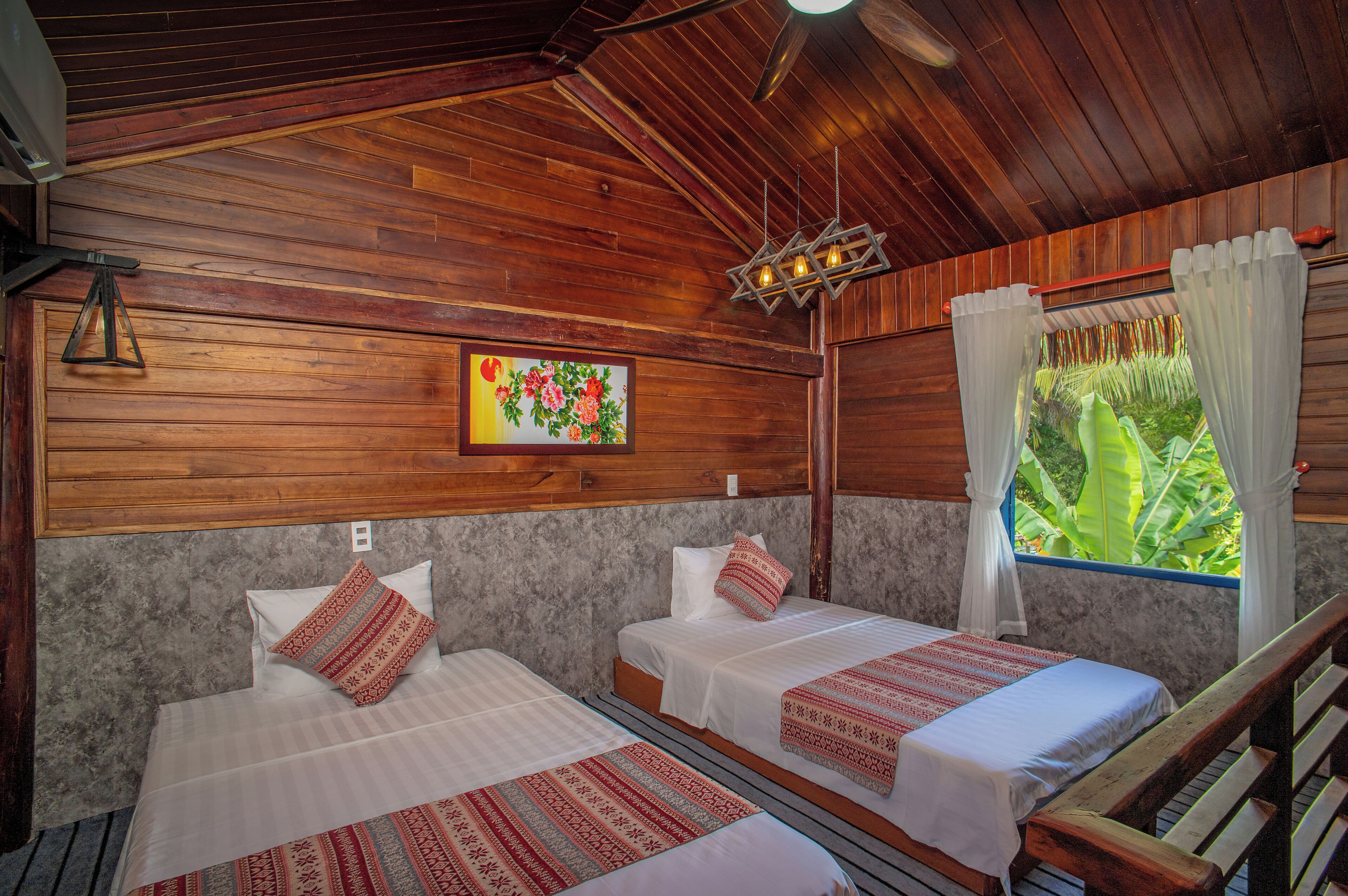 A room with two beds, wooden ceiling, a painting, and a window with curtains.