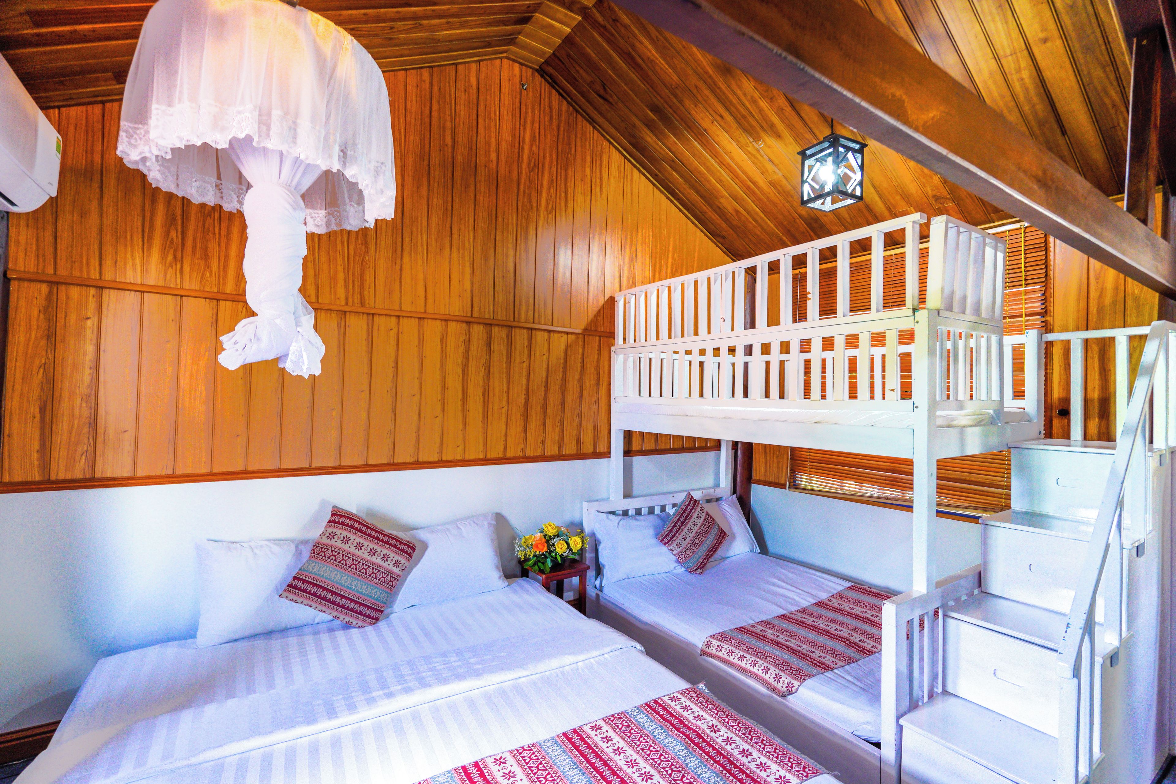 A bunk bed room with a wooden ceiling, a hanging light fixture, and a small table with flowers.