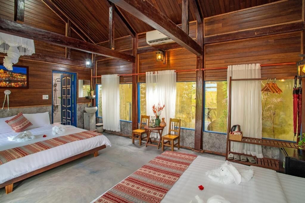 A wooden room with a bed, a small table, chairs, and a window with curtains.