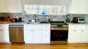 A modern kitchen with white cabinets, a dishwasher, a stove, and a window overlooking a wooded area. - 3 Bedroom Dream: Hudson Valley views, Woodbury Commons, West Point & Storm King (Cornwall)