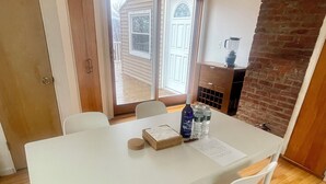 A dining area with a white table and four chairs, a brick wall, and a door leading outside. - 3 Bedroom Dream: Hudson Valley views, Woodbury Commons, West Point & Storm King (Cornwall)