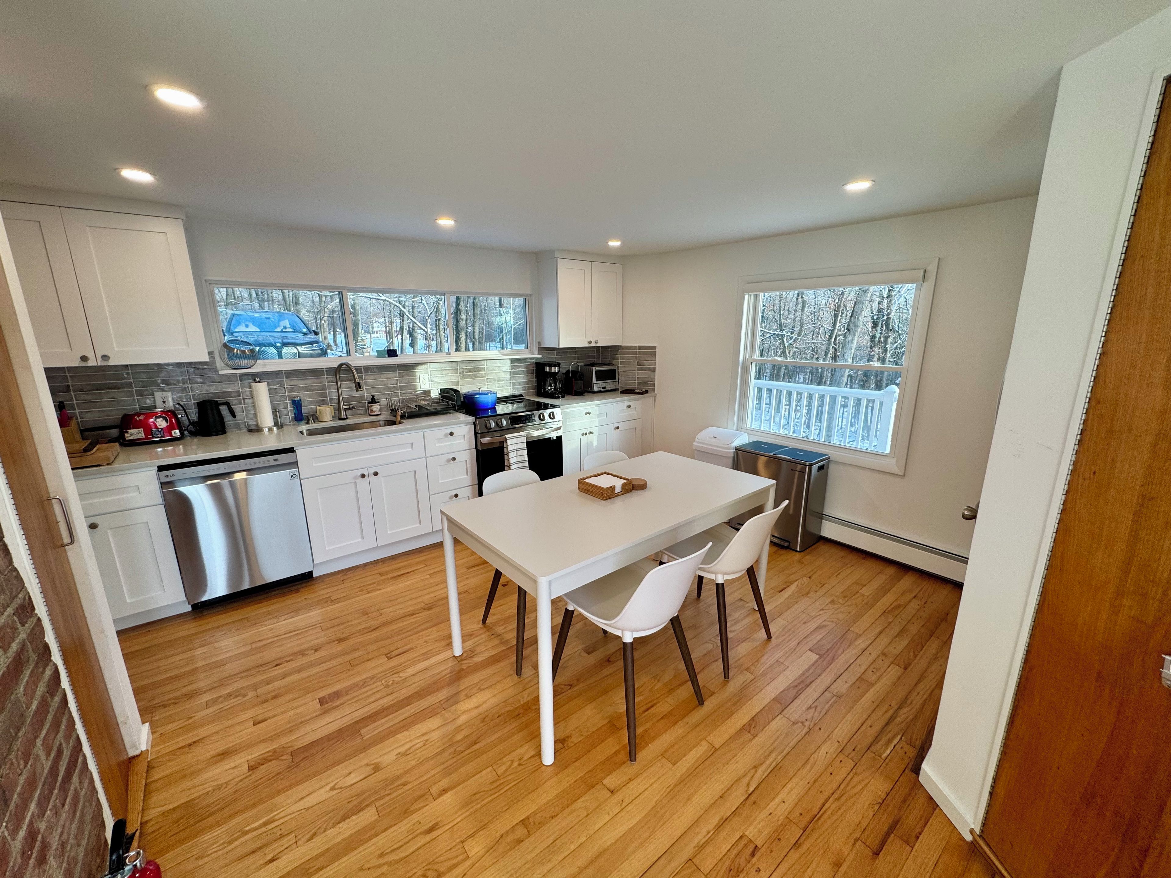 A compact kitchen with white cabinets, a dishwasher, a stove, and a dining area with a table and chairs.