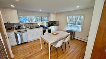 A compact kitchen with white cabinets, a dishwasher, a stove, and a dining area with a table and chairs.
