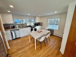 A compact kitchen with white cabinets, a dishwasher, a stove, and a dining area with a table and chairs. - 3BR Home with Fireplace & Hudson Valley views near Woodbury Commons, West Point (Cornwall)