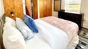 Ein Schlafzimmer mit Bett, Kommode, Lampe und Fenster.
