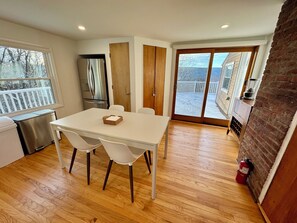 A modern kitchen with a stainless steel refrigerator, a white dining table with chairs, and a sliding glass door leading to a balcony.