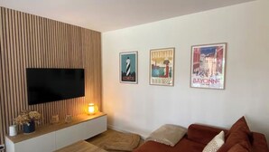 Een moderne woonkamer met een flatscreen-tv, een wand van houten panelen, een witte bank en drie ingekaderde posters.
