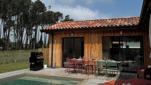 Een houten huis met pannendak, een zwembad en een terras met tuinmeubilair.