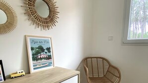 Een kamer met een houten dressoir, een rieten stoel, een ingelijste foto en twee spiegels aan de muur.
