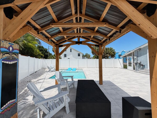 A covered outdoor area with a pool, lounge chairs, and a tiki-themed decoration.