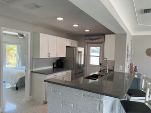 A modern kitchen with white cabinets, a stainless steel refrigerator, and a granite countertop island.
