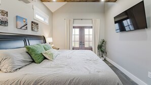 Ein Schlafzimmer mit einem großen Bett, einem Flachbildfernseher, einem Fenster mit Vorhängen und Bildern an der Wand.