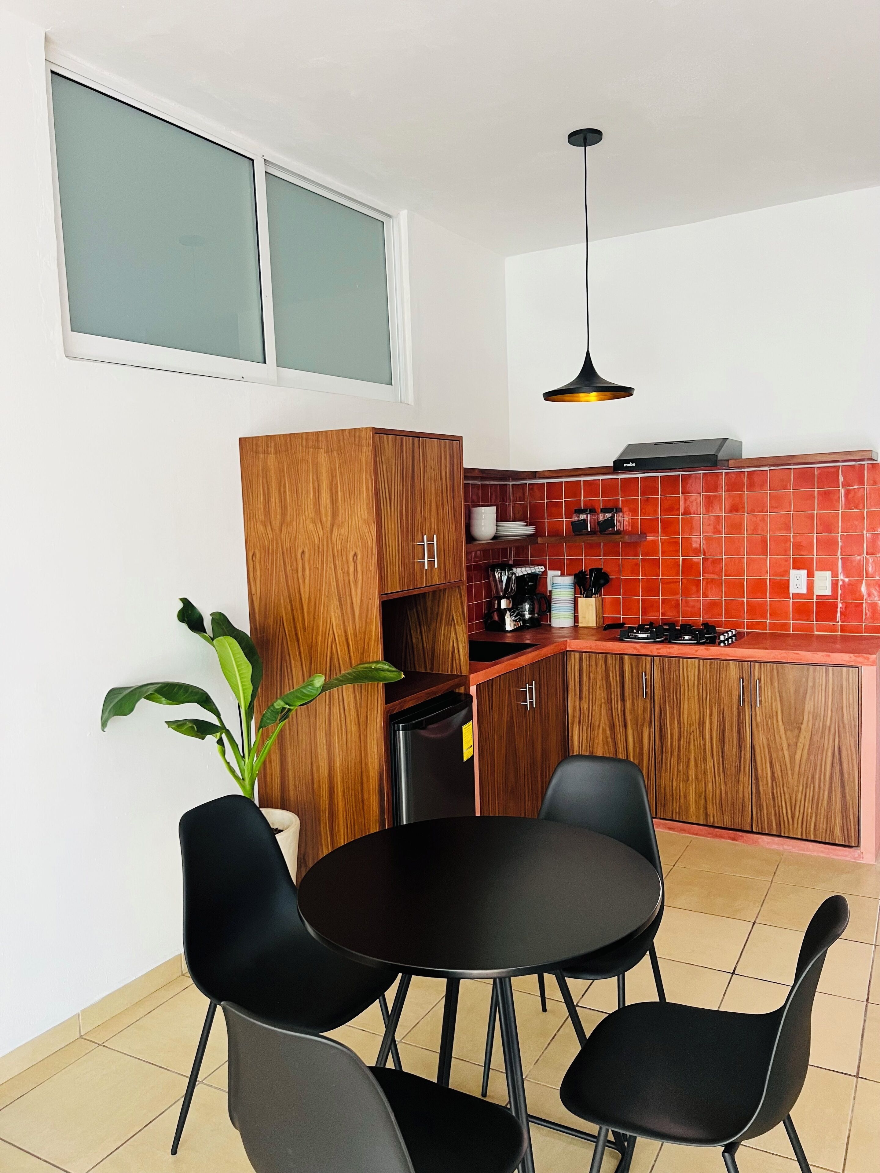A compact kitchen with wooden cabinets, a black refrigerator, a gas stove, and a dining table with four chairs.